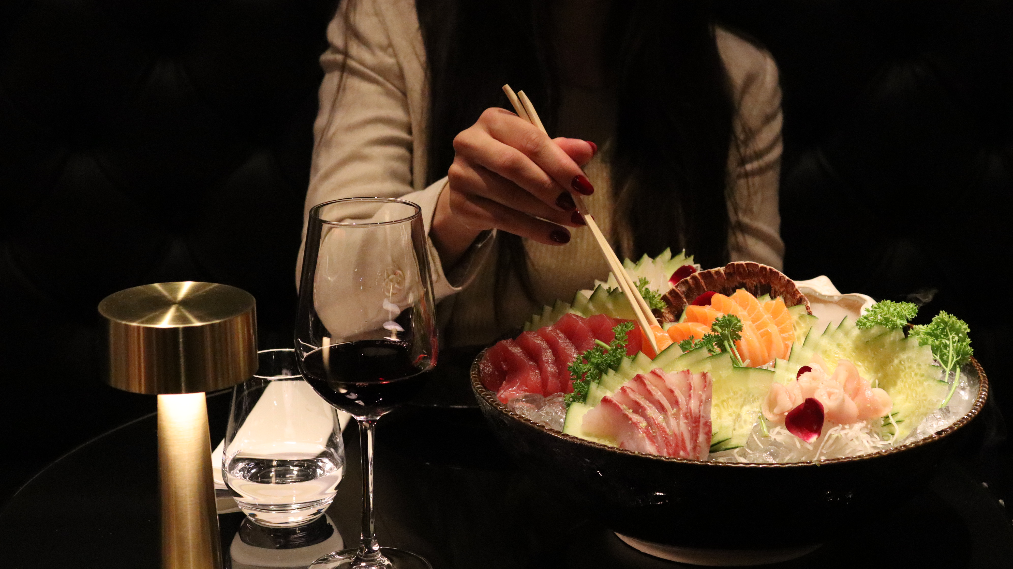 Pessoa usando hashis para pegar sushi de um prato grande com sashimi e vegetais